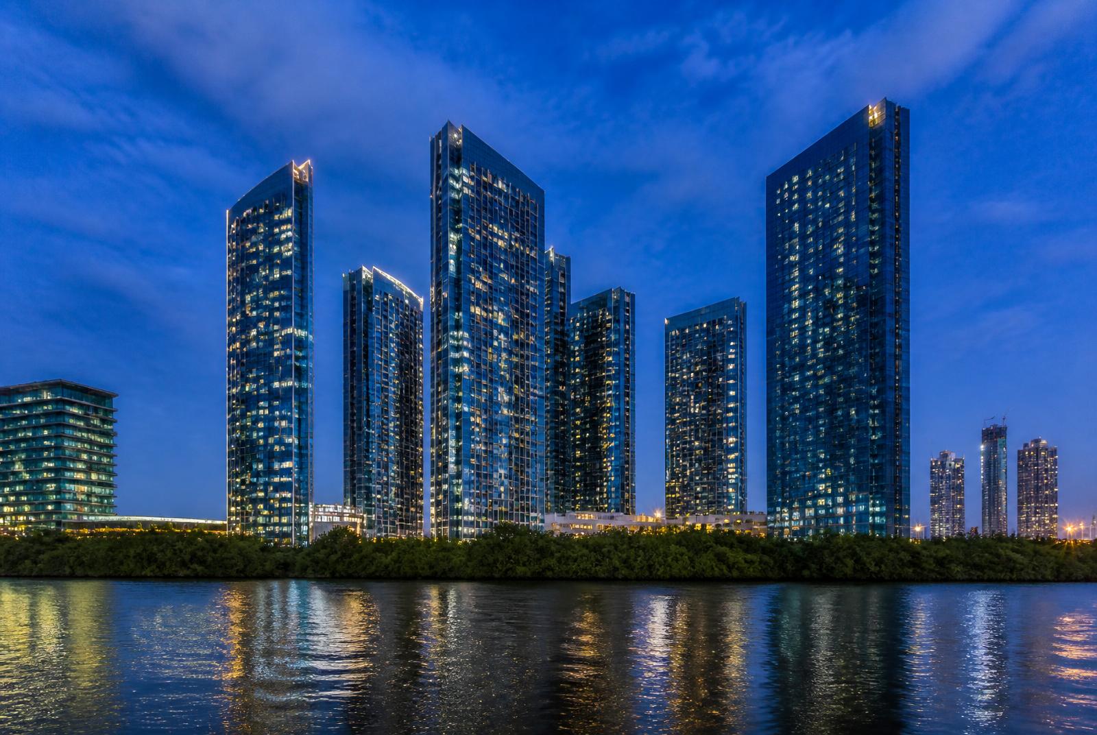 Verlichte woontorens op Al Reem Island in Abu Dhabi gezien vanaf het water tijdens het blauwe uur